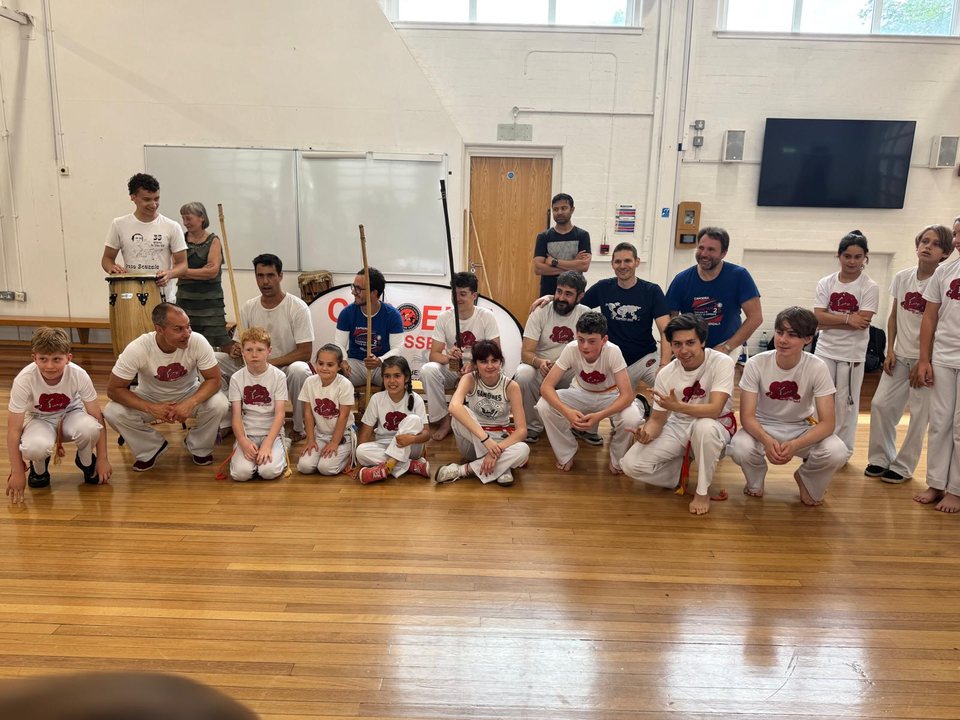 Children and adults from the capoeira school gather for a group photograph in the training hall.